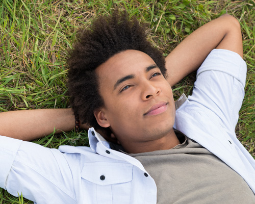 a person lying on the grass with his hands behind his head